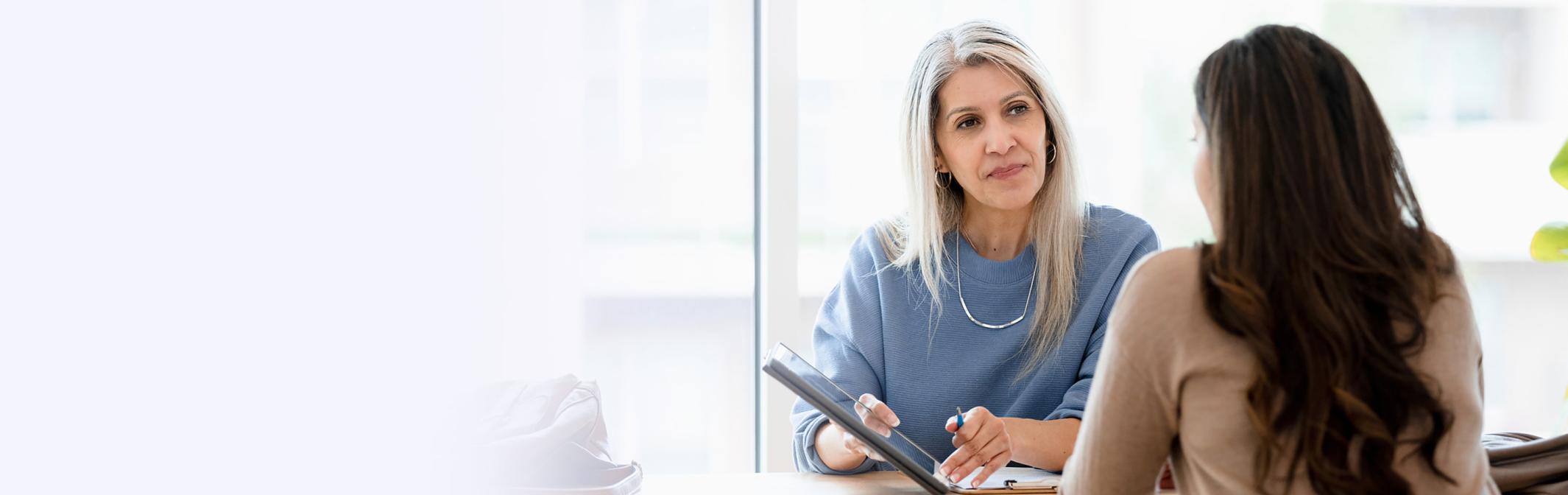 two women sitting at a table looking at a tablet